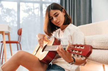 Klasik gitar çalmayı öğreniyorum. Günlük giysiler içinde güzel bir kadın evde, yurt odasında..