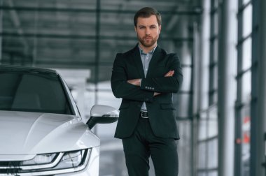 Siyah takım elbiseli adam otomobilin yanındaki araba galerisinde..