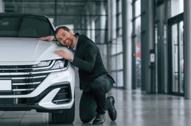 Aracı kucakla. Siyah takım elbiseli adam otomobilin yanındaki araba galerisinde..