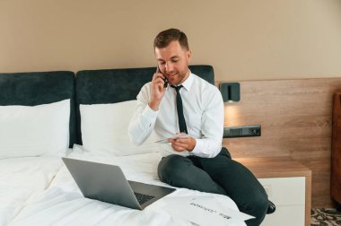 Biletleri tutmak, dizüstü bilgisayarla yatakta oturup telefonla konuşmak. İş adamı içeride, otel odasında..