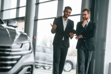 Otomobilden bahsediyoruz. Adam galeride müşteriye danışıyor..