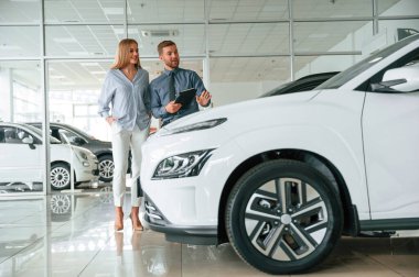 Otomobili seçiyorum. Resmi elbiseli adam elektrikli arabalı kadın müşteriyle birlikte..