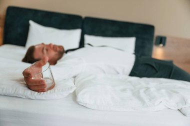 Elindeki boş bardak, yatağa uzanmış, yorgun. İş adamı içeride, otel odasında..