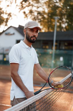 Ağın yanında raketle bekliyorum. Genç adam güneşli bir günde tenis kortunda..