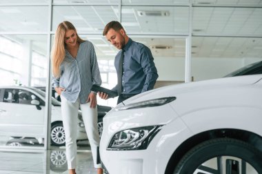 Müşteriye yardım ediyorum. Resmi elbiseli adam elektrikli arabalı bir kadınla birlikte..