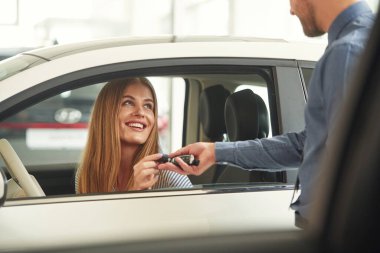 Anahtarları veriyorum. Resmi elbiseli adam elektrikli arabalı kadın müşteriyle birlikte..