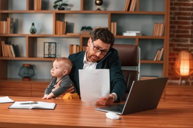Meşgul baba. Resmi kıyafetli bir iş adamı içeride çalışıyor. Yürüyen bebekle.