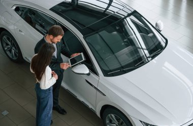 Adam araba galerisindeki kadın müşteriye yeni otomobili gösteriyor..