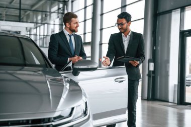 Otomobilin yanında dikilip konuşmak. Adam galeride müşteriye danışıyor..