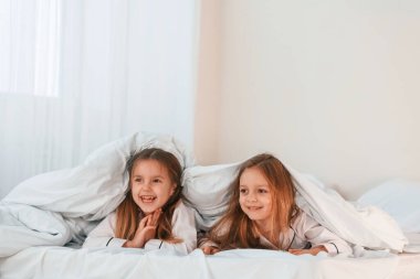 Yatağın üzerindeki battaniyenin altında. İki küçük kız evcil odada oynuyorlar ve eğleniyorlar..