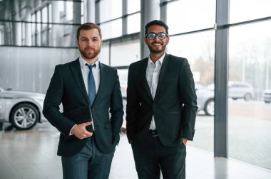 Ayakta ve gülümsüyor. İki işadamı araba galerisinde birlikte çalışıyorlar..