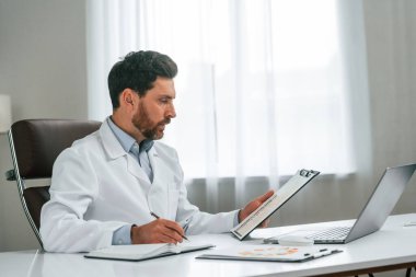 Belgeyi okuyorum. Resmi kıyafetli doktor dolapta çalışıyor..