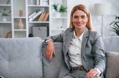 Ön manzara. Resmi elbiseli kadın evde, kanepede oturuyor..