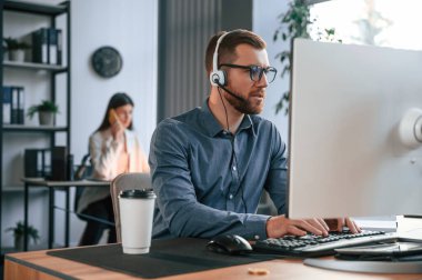 Adam bilgisayar kullanıyor. Modern ofiste iki çalışan birlikte çalışıyor..