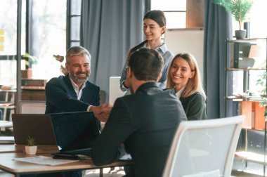 Masanın yanında oturuyor. Bir grup iş adamı modern ofiste çalışıyor..