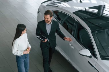 Üst Manzara. Adam araba galerisindeki kadın müşteriye yeni otomobili gösteriyor..