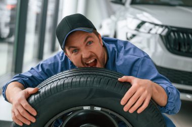 Eğleniyor, gülümsüyor, lastiklerle. Mavi üniformalı adam araba servisinde çalışıyor..