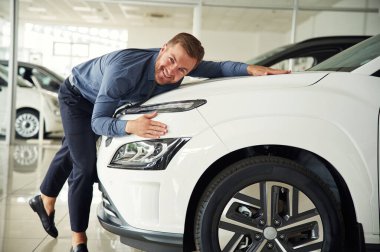 Yeni otomobili kucaklıyorum. Yakışıklı araba galerisi çalışanı elektrikli araçla çalışıyor..