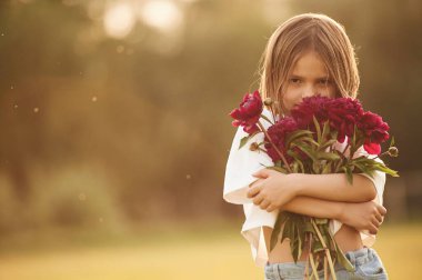 Portre, ayakta ve elinde kırmızı çiçekler var. Küçük kız gündüz vakti yaz tarlasında..