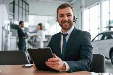 Elinde grafik tabletle. Araba galerisinde üç kişi birlikte çalışıyor..