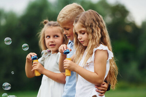 With bubbles. Kids are having fun on the field at daytime together.