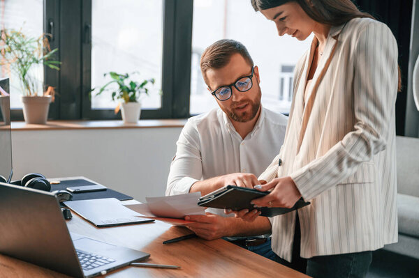 Женщина держит планшет, анализирует информацию. Два сотрудника работают вместе в современном офисе.