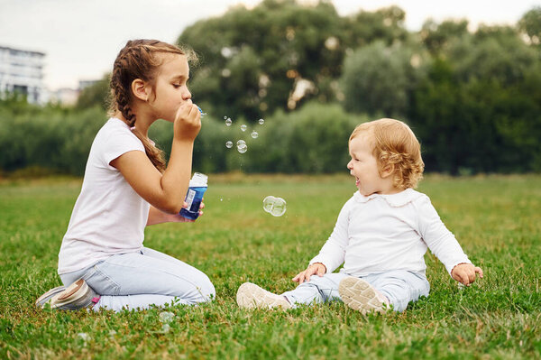 Girl is playing with bubbles while her little sister is sitting.