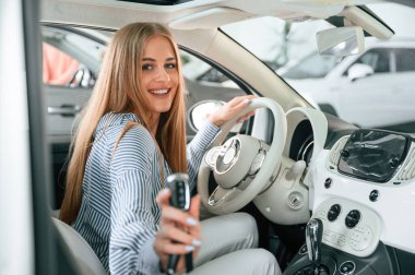 Yeni otomobilin anahtarlarını gösteriyor. Güzel kadın modern arabasıyla içeride..