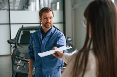 Belgeyi veren adam. Genç bir kadın garajda araba tamircisini ziyaret ediyor. Onarım servisi.