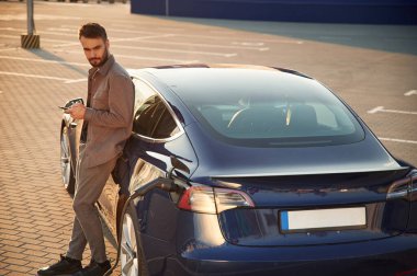 Otomobilin arka görüntüsü. Adam dışarıda elektrikli arabasının yanında duruyor..