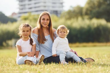 Anne ve iki küçük kızı yeşil alanda oturuyor..