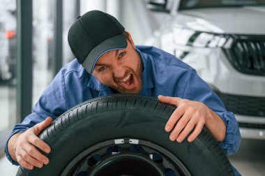 Eğleniyor, gülümsüyor, lastiklerle. Mavi üniformalı adam araba servisinde çalışıyor..