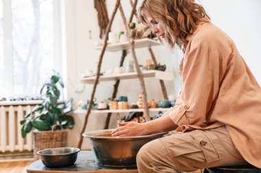 Kadın oturuyor ve çömlekçide el yapımı bir seramik kase yapıyor..