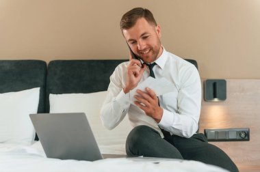 Bilet bilgilerini okumak, telefonla konuşmak. İş adamı içeride, otel odasında..