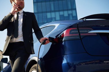 İş görüşmesi, telefonla konuşmak. Adam dışarıda elektrikli arabasının yanında duruyor..