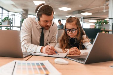 İnsan yardım ediyor, öğretiyor. Küçük kız, insanların birlikte çalıştığı ofiste..