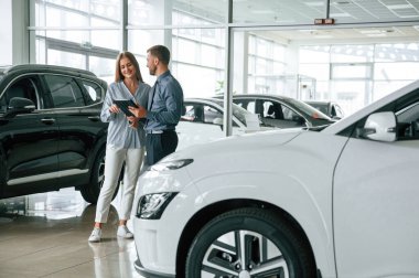Güzel beyaz bir otomobil. Resmi elbiseli adam elektrikli arabalı kadın müşteriyle birlikte..