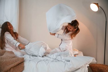 Yurt içi odada, yatağın üstünde. Yastık savaşı oynuyoruz. İki küçük kız yurt odasında birlikte eğleniyorlar..