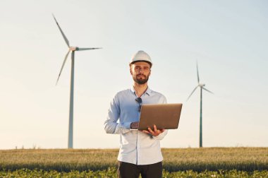 Ellerinde dizüstü bilgisayarla. Servis mühendisi yel değirmenleriyle sahada..