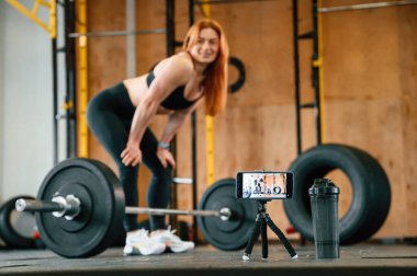 Halterli. Akıllı telefondan video çekiyoruz. Güzel, güçlü kadın spor salonunda..