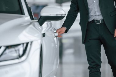 Yeni beyaz renkli otomobilin kapısını açan takım elbiseli adamın yakın görüntüsü.