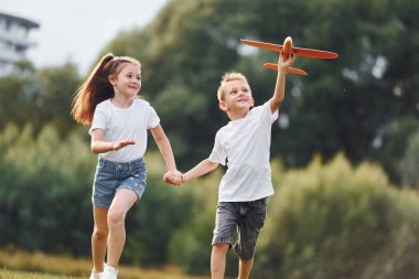 Ön manzara. Erkek ve kız yeşil alanda oyuncak uçakla oynuyorlar..