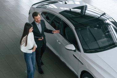 Üst Manzara. Adam araba galerisindeki kadın müşteriye yeni otomobili gösteriyor..