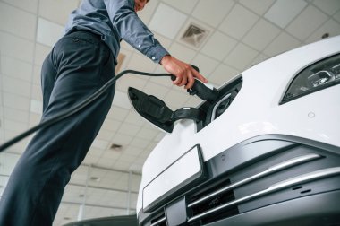 Şarj aletini takıyorum. Yakışıklı araba galerisi çalışanı elektrikli araçla çalışıyor..