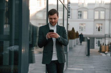 Akıllı telefonla sosyal medyayı kullanmak. Resmi kıyafetli yakışıklı dışarıda, iş binasının yanında..