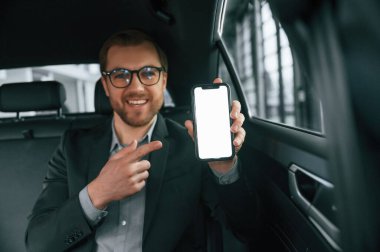 Akıllı telefonu tutuyorsun. Resmi iş elbiseli adam modern otomobilde oturuyor..