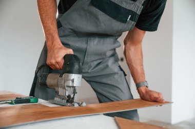 Tahtayı kesmek için elektrikli makineyi kullanmak. Adam yeni kaplamalı ahşap döşeme kuruyor..