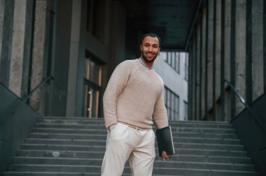 Dizüstü bilgisayarı elimde tutuyorum. Yakışıklı siyah adam iş binasının yakınında dışarıda..