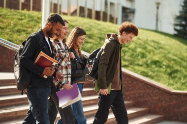 Yürüyorum, elimde not defterleri var. Gündelik giysiler içinde dört genç dışarıda beraberler..
