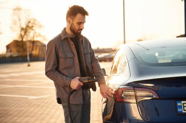 - Otoparkta. Otomobili şarj ediyorum. Adam dışarıda elektrikli arabasının yanında duruyor..